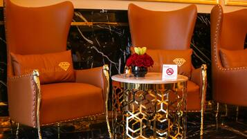 A luxurious room with two brown leather armchairs, a round table with a gold geometric base, and a vase with red roses.