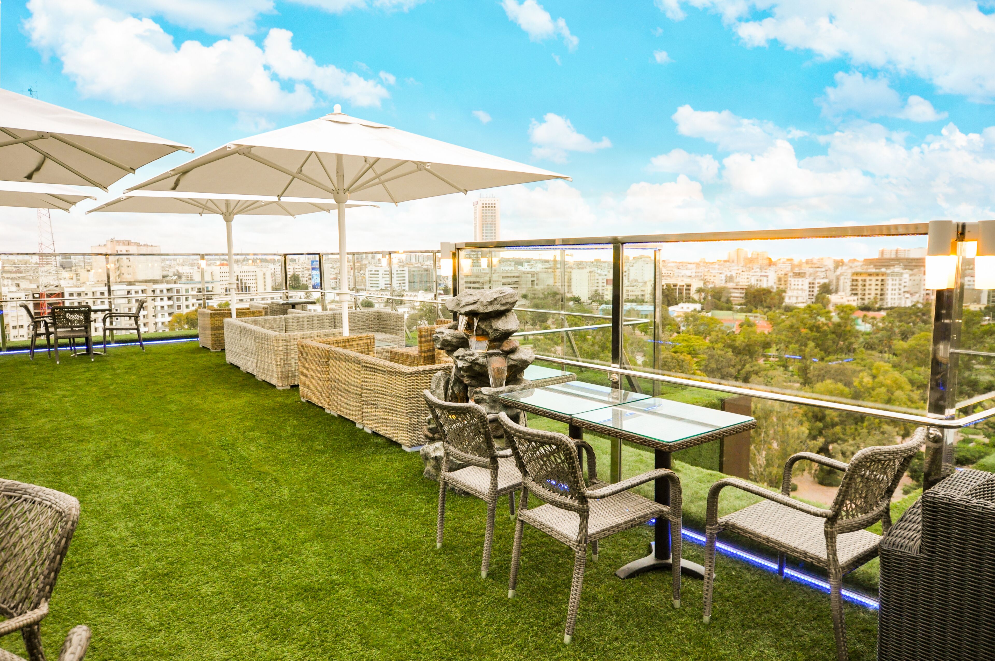 A rooftop terrace with wicker furniture, white umbrellas, and a view of the city.