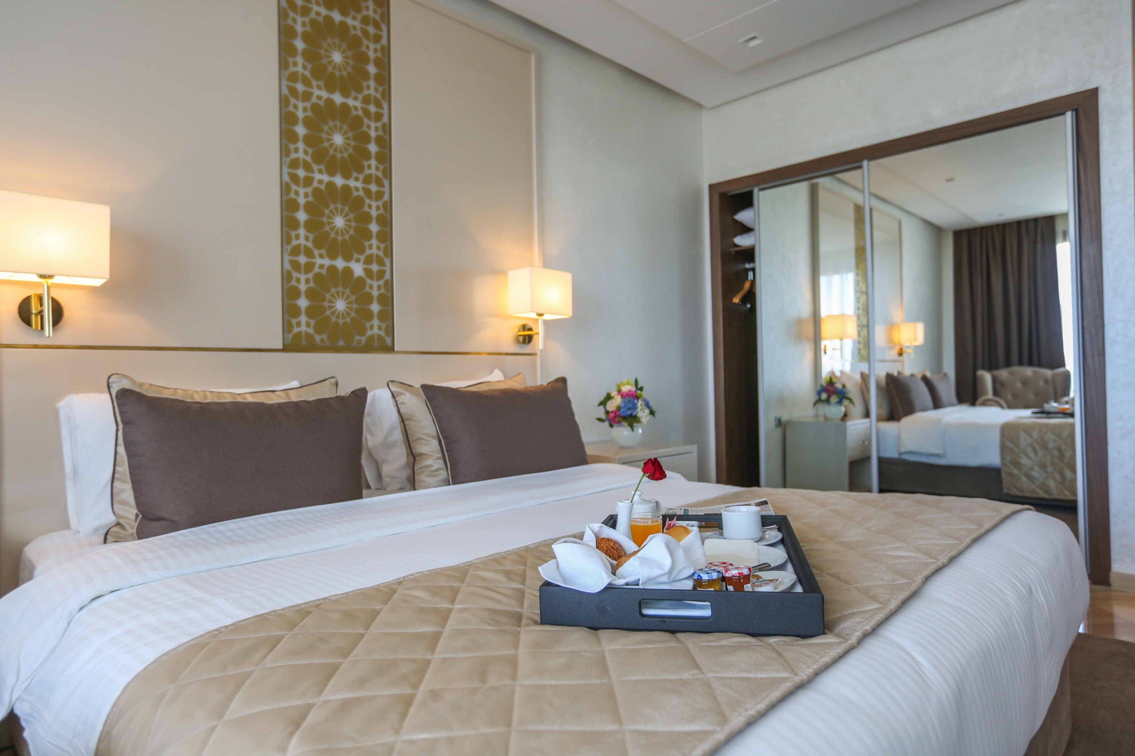 A hotel room with a large bed, a tray of breakfast items, and a mirror reflecting the room.