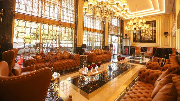 Een luxe lobby met zachte zitplaatsen, een weelderige kroonluchter en grote ramen met decoratieve roosters.