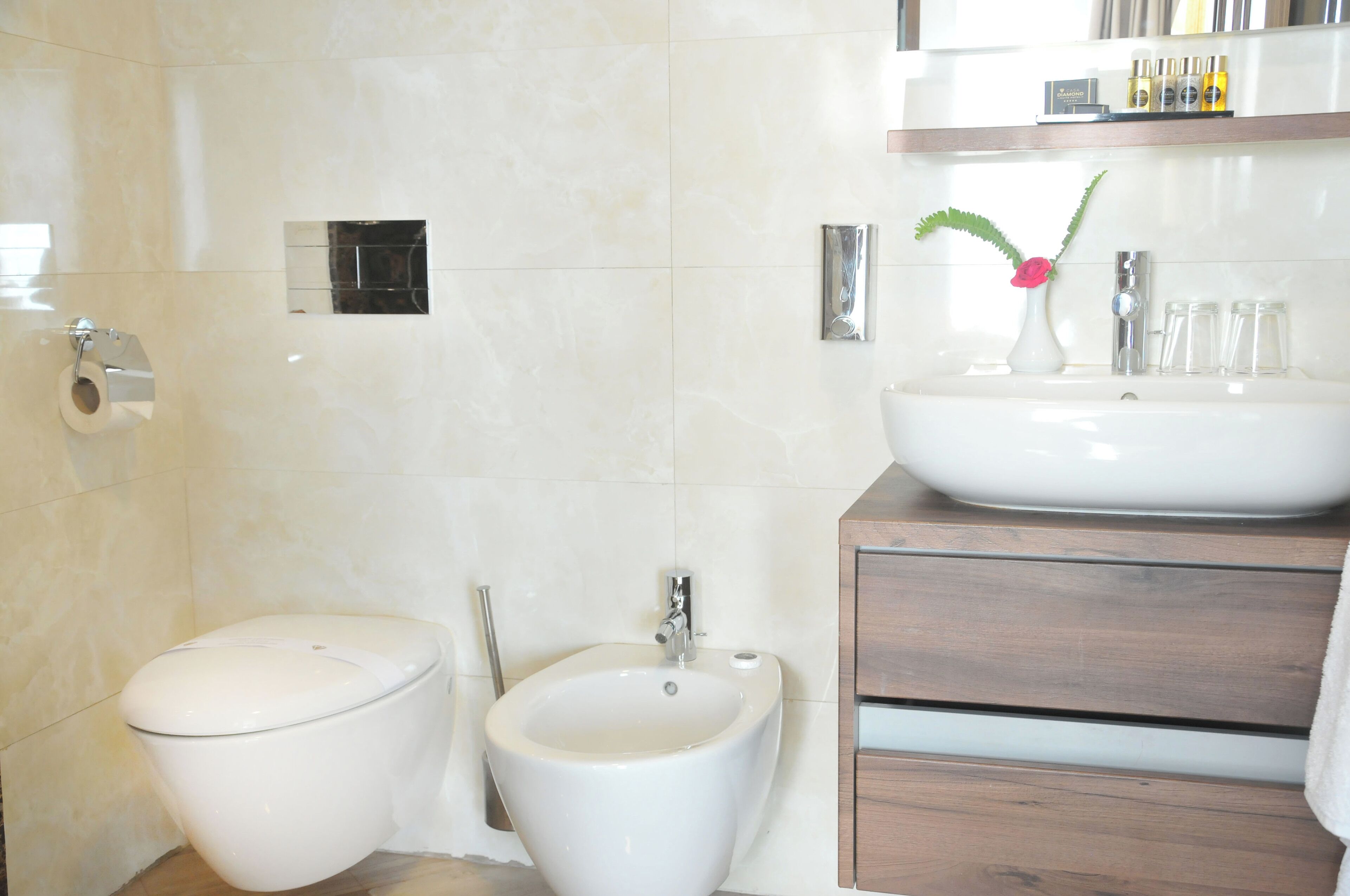 Un baño moderno con inodoro, bidé y lavamanos con un florero.