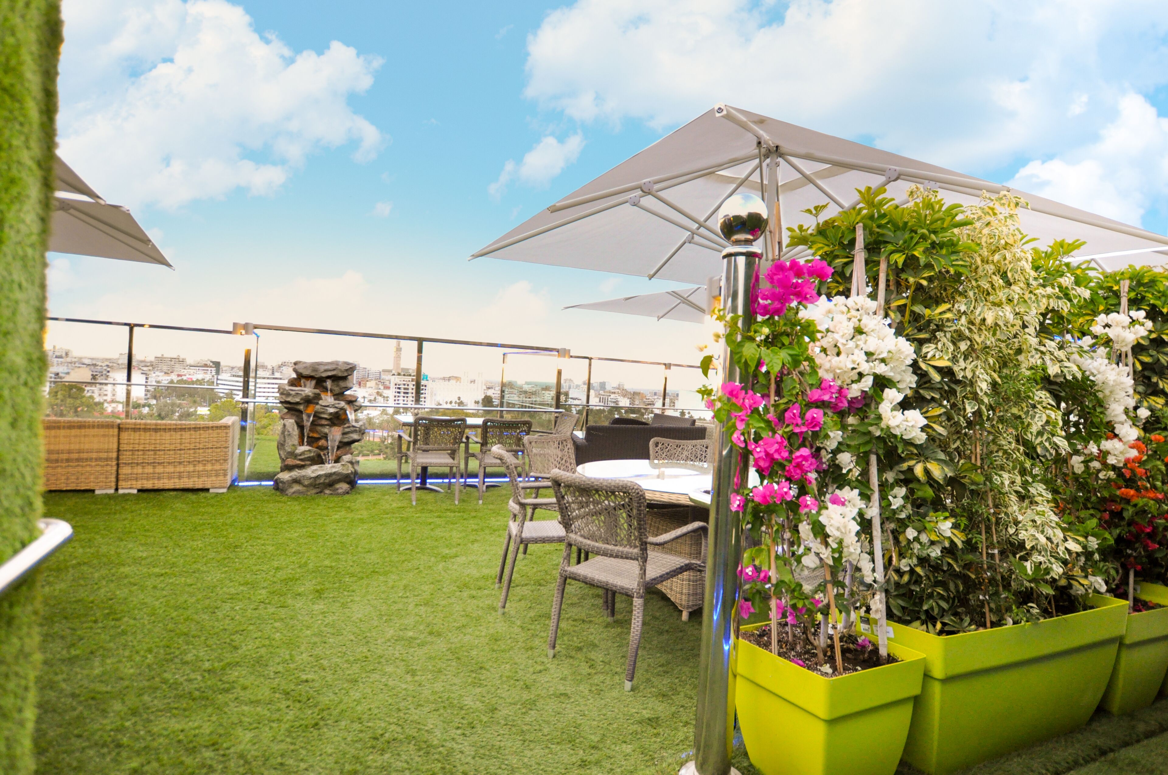 A rooftop terrace with green artificial grass, wicker furniture, and potted plants.
