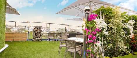 A rooftop terrace with green artificial grass, wicker furniture, and potted plants.
