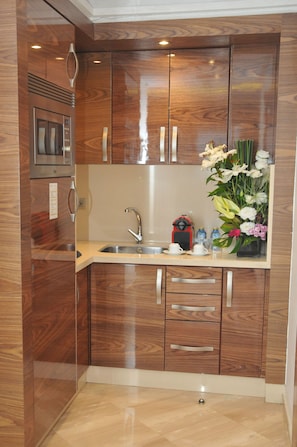 A compact kitchen with wooden cabinetry, a built-in microwave, a sink, and a small countertop with a coffee maker and decorative flowers.