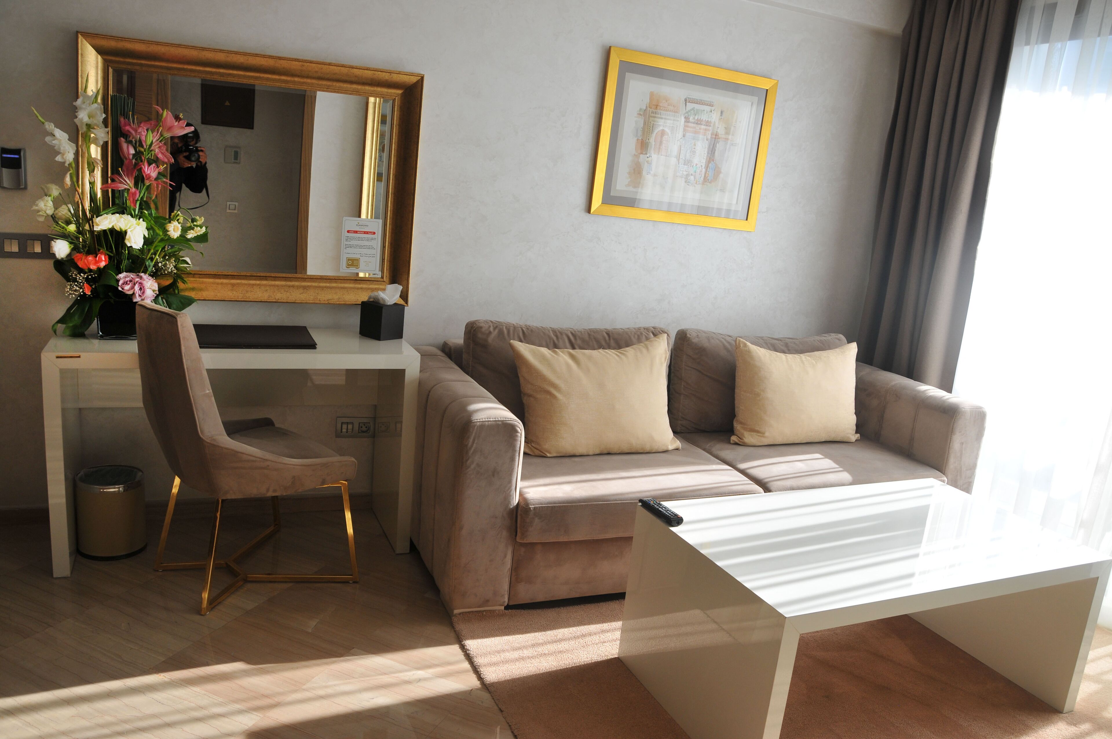 Una habitación de hotel moderna con sofá, escritorio, silla, espejo y un cuadro en la pared.