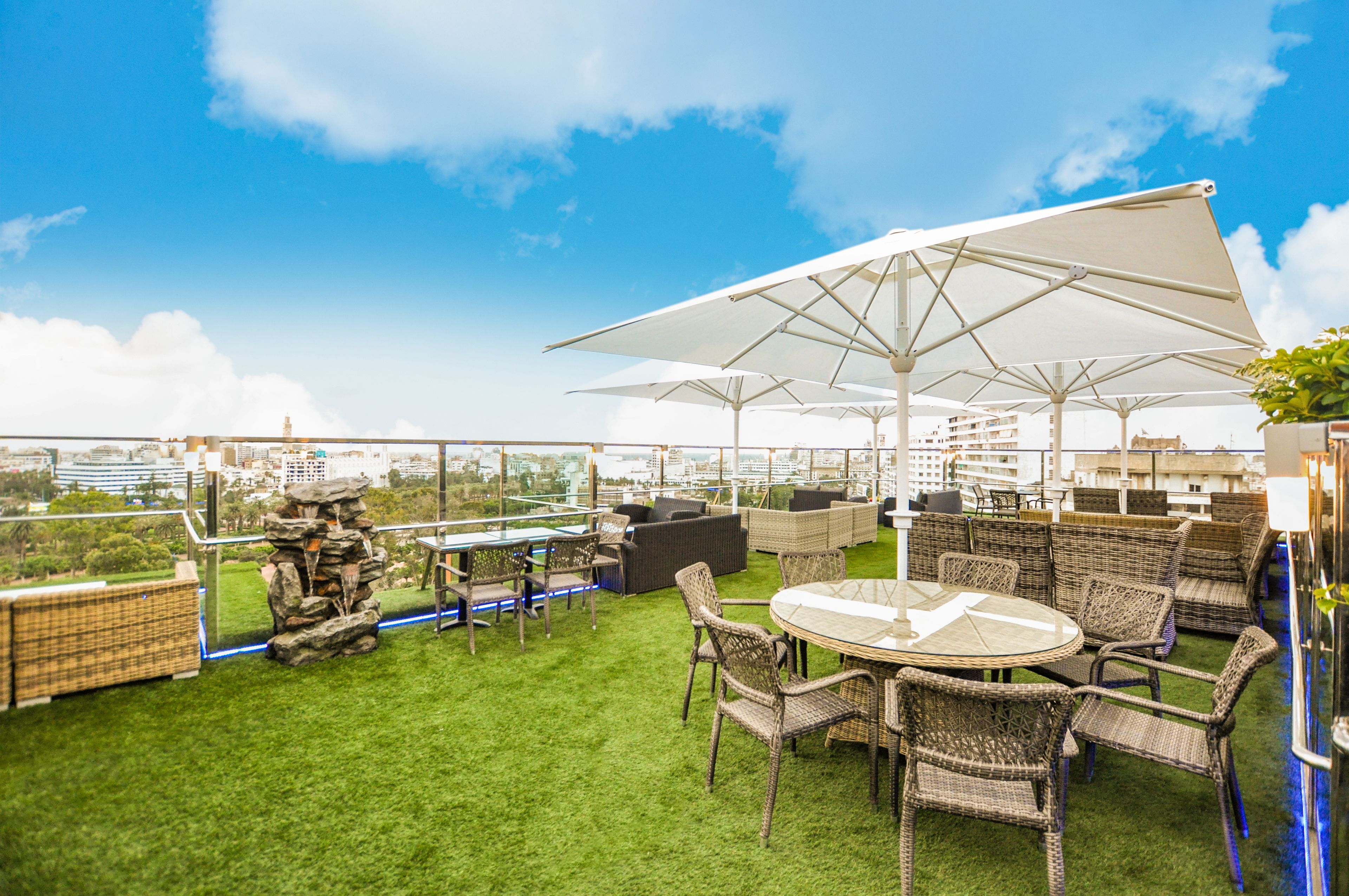 Een terras op het dak met rieten meubels, een ronde tafel en grote parasols.