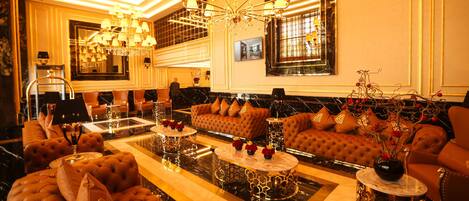 A luxurious lobby with a large sofa set, multiple tables, and a grand chandelier.
