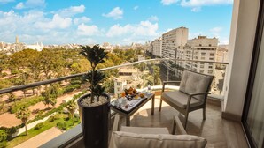 Een balkon met uitzicht op een stadsbeeld, een bloempot en een tafel met ontbijtartikelen.