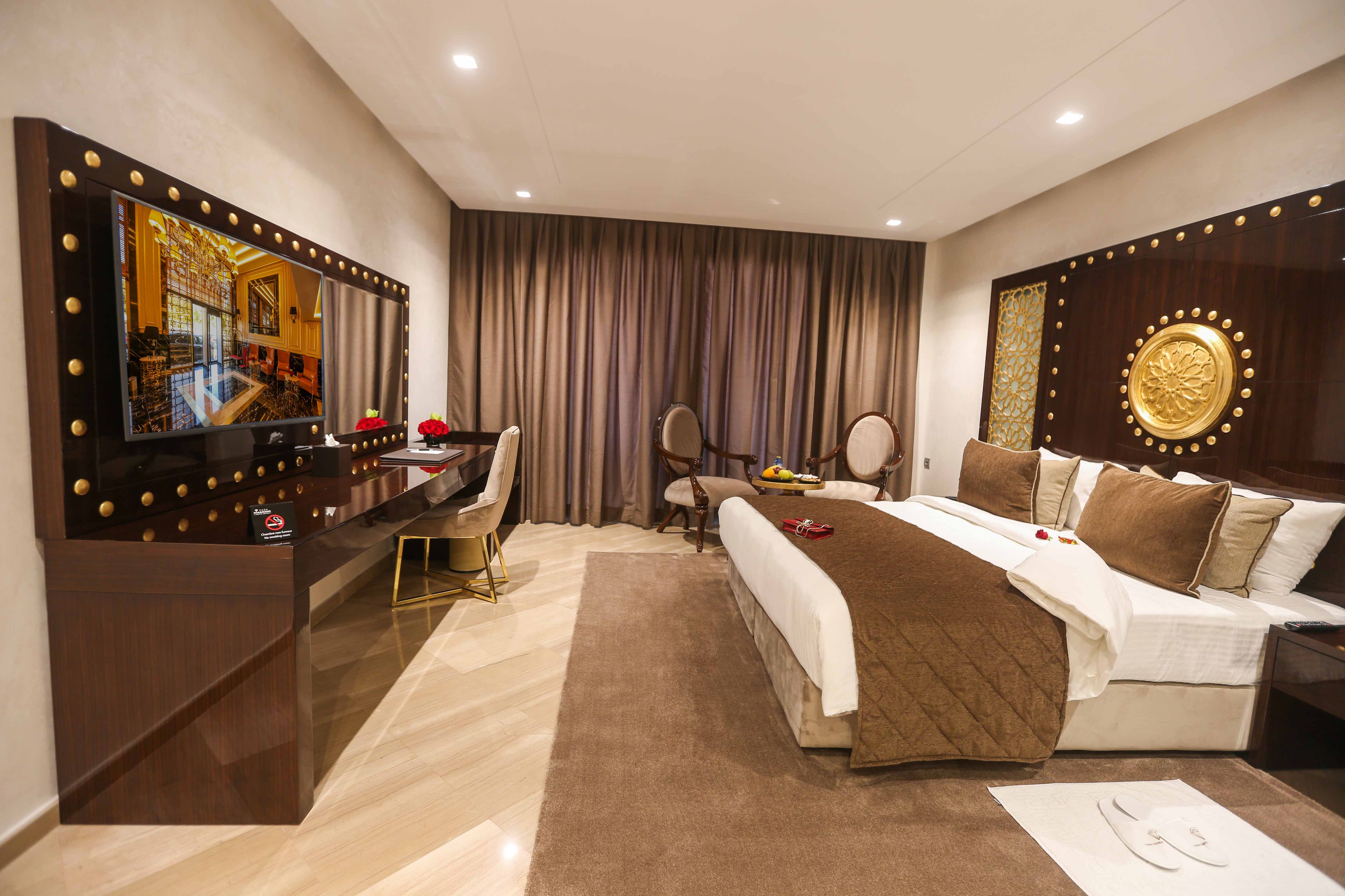 A hotel room with a large bed, a desk with a computer, a TV, and a mirror.