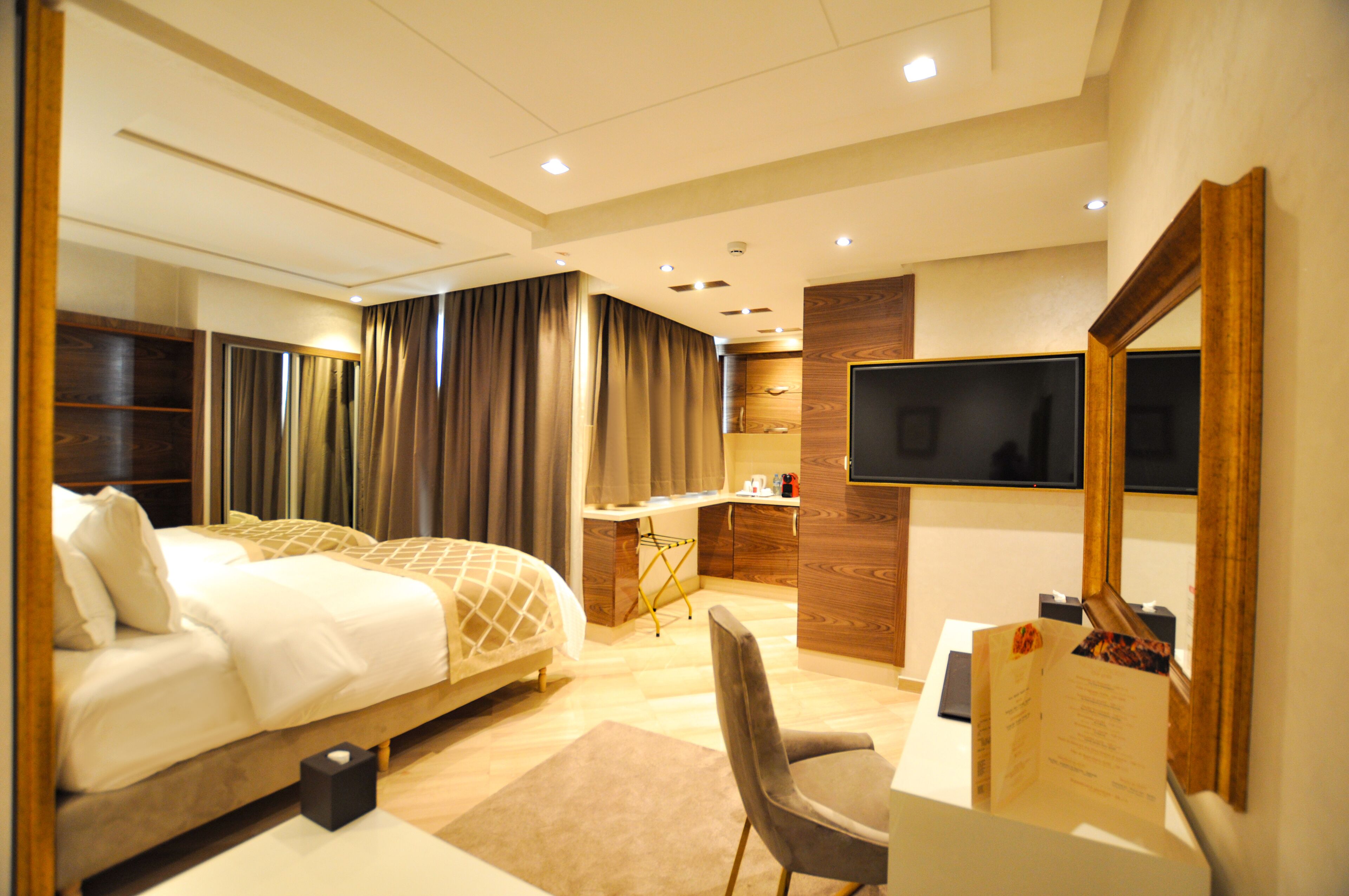 A modern hotel room with a large bed, a desk, a chair, a flat-screen TV, and a large mirror.