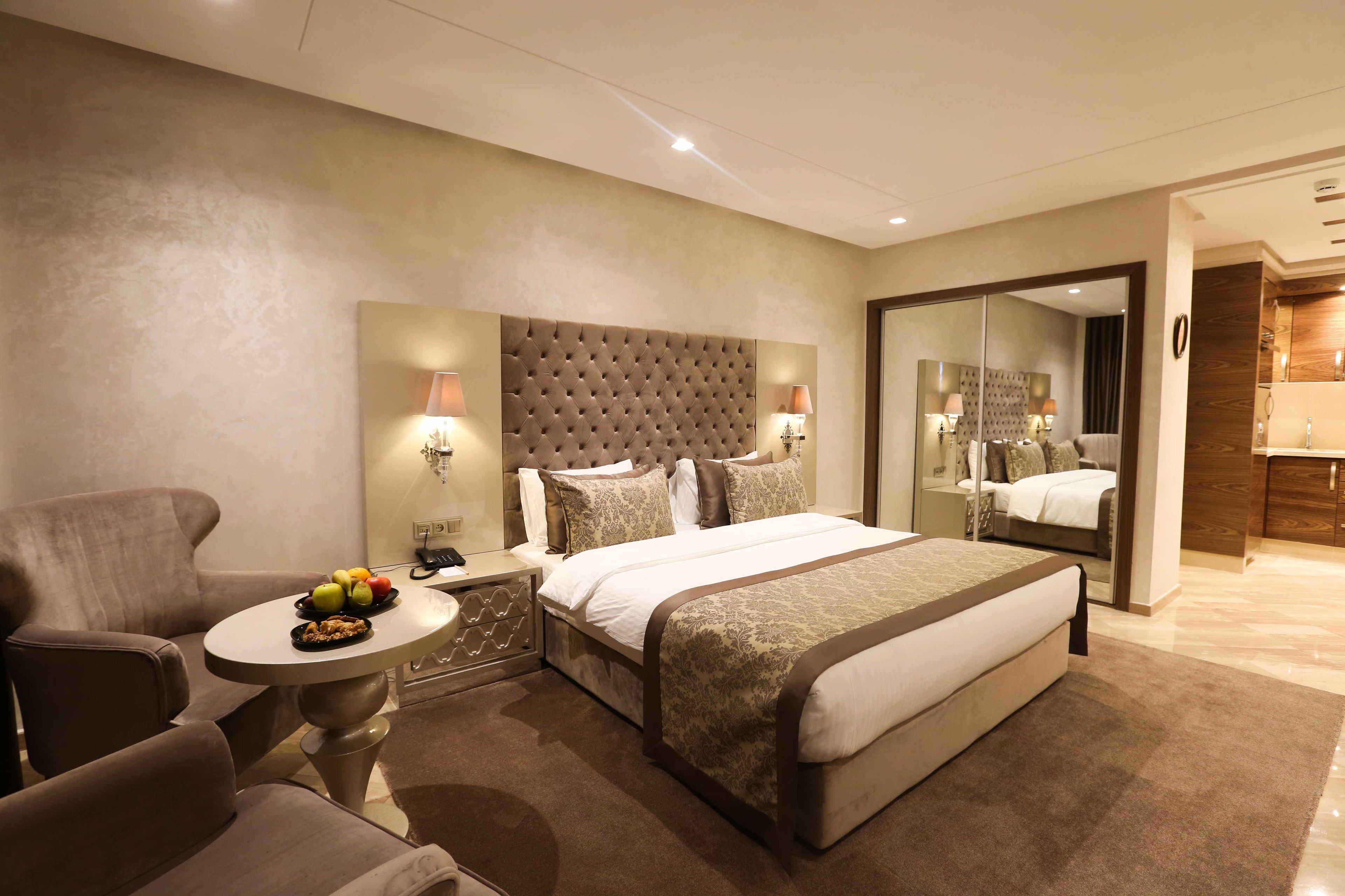 A modern hotel room with a large bed, a sitting area with a small table, and a large mirror.