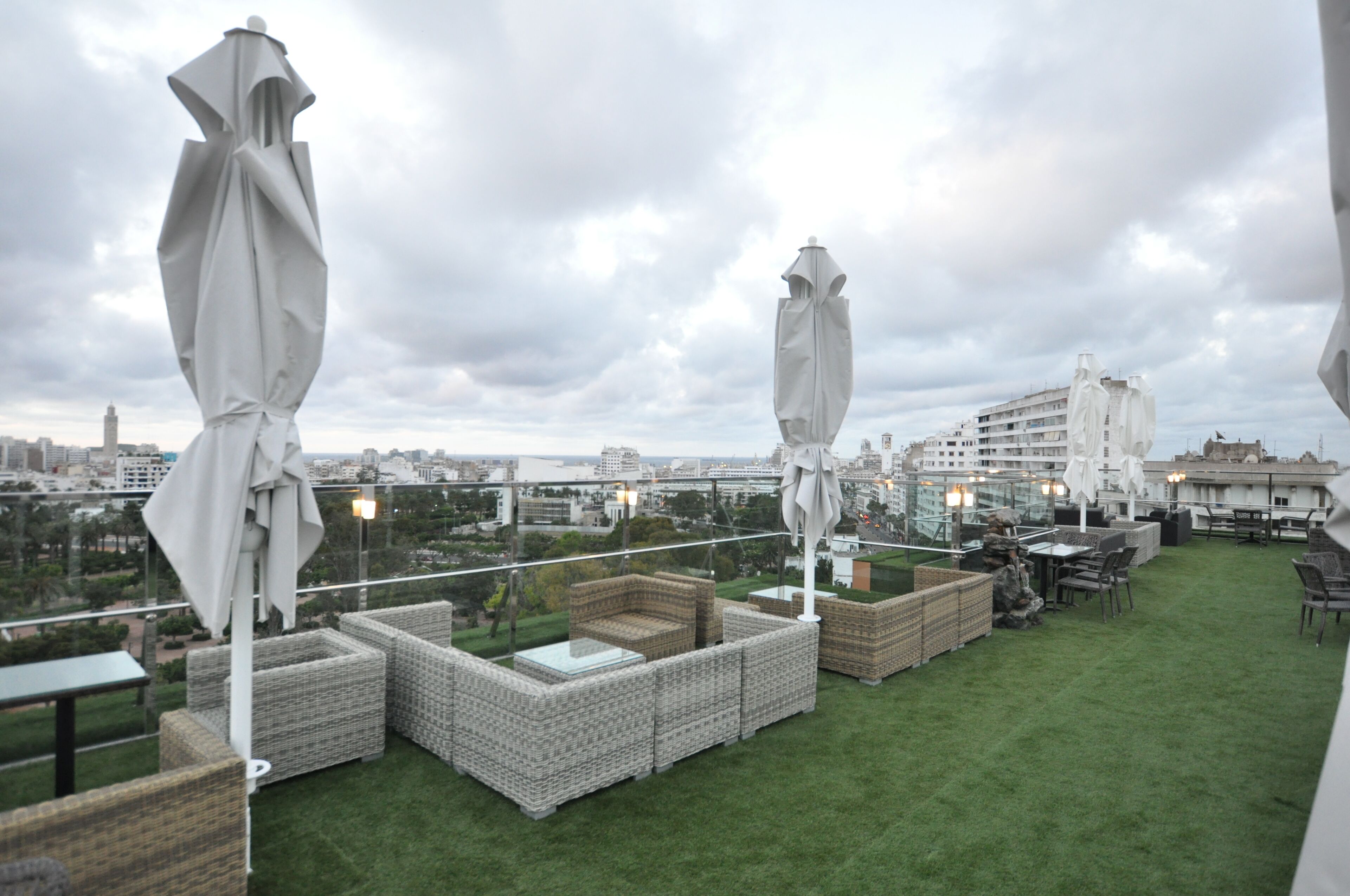 Una terraza en la azotea con mobiliario de mimbre y sombrillas blancas, que ofrece vistas de la ciudad.