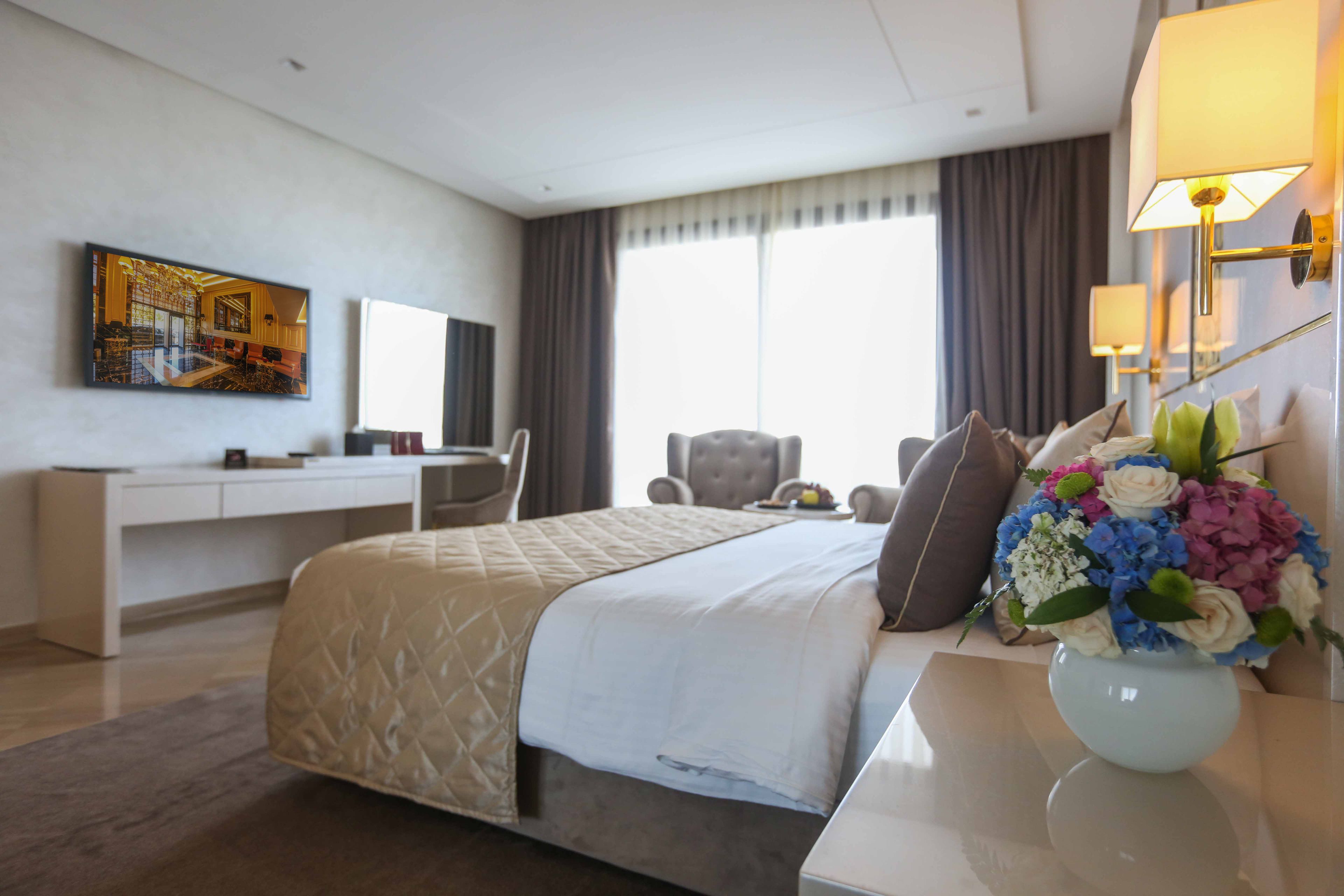 A hotel room with a bed, a desk, a chair, a TV, and a vase of flowers.