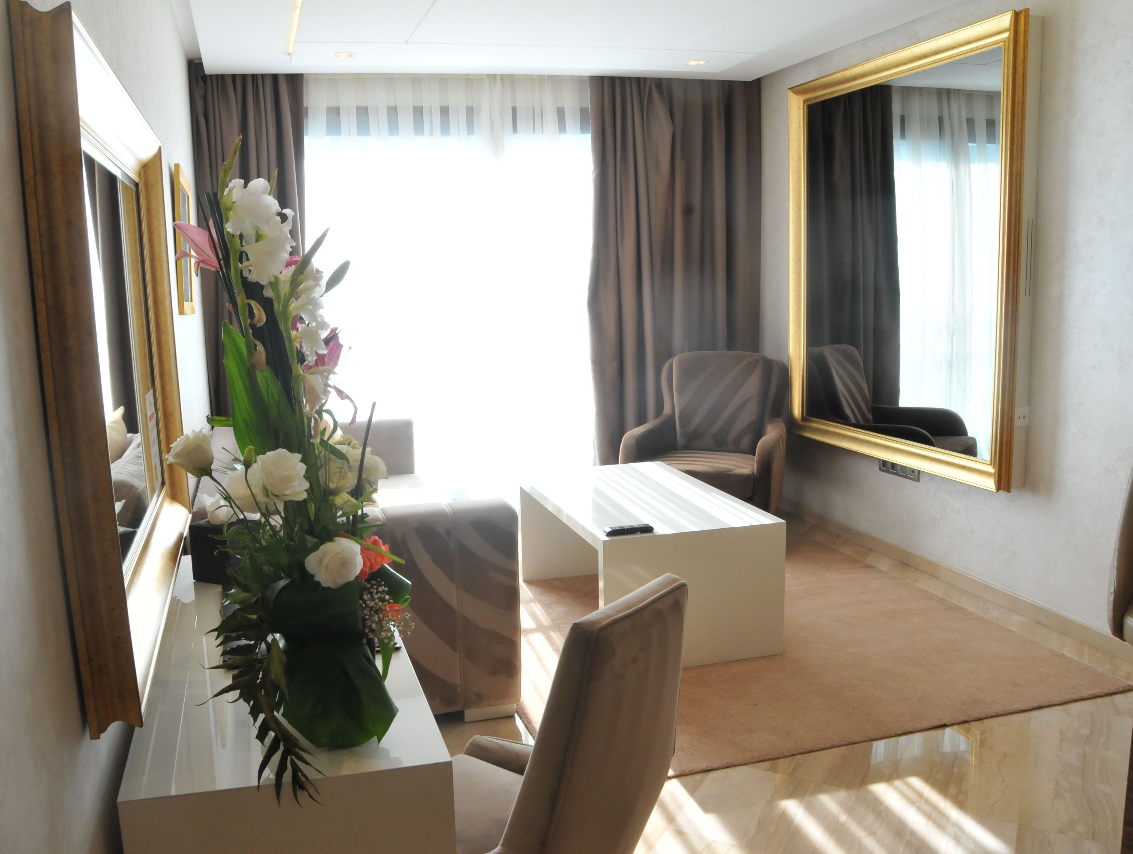 Habitación de hotel con un espejo grande, un escritorio con un florero, una silla y un sofá.