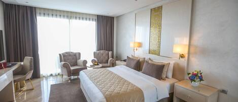 Una habitación de hotel con una cama grande, dos sillones, un escritorio y una mesita de noche con lámpara y un jarrón de flores.