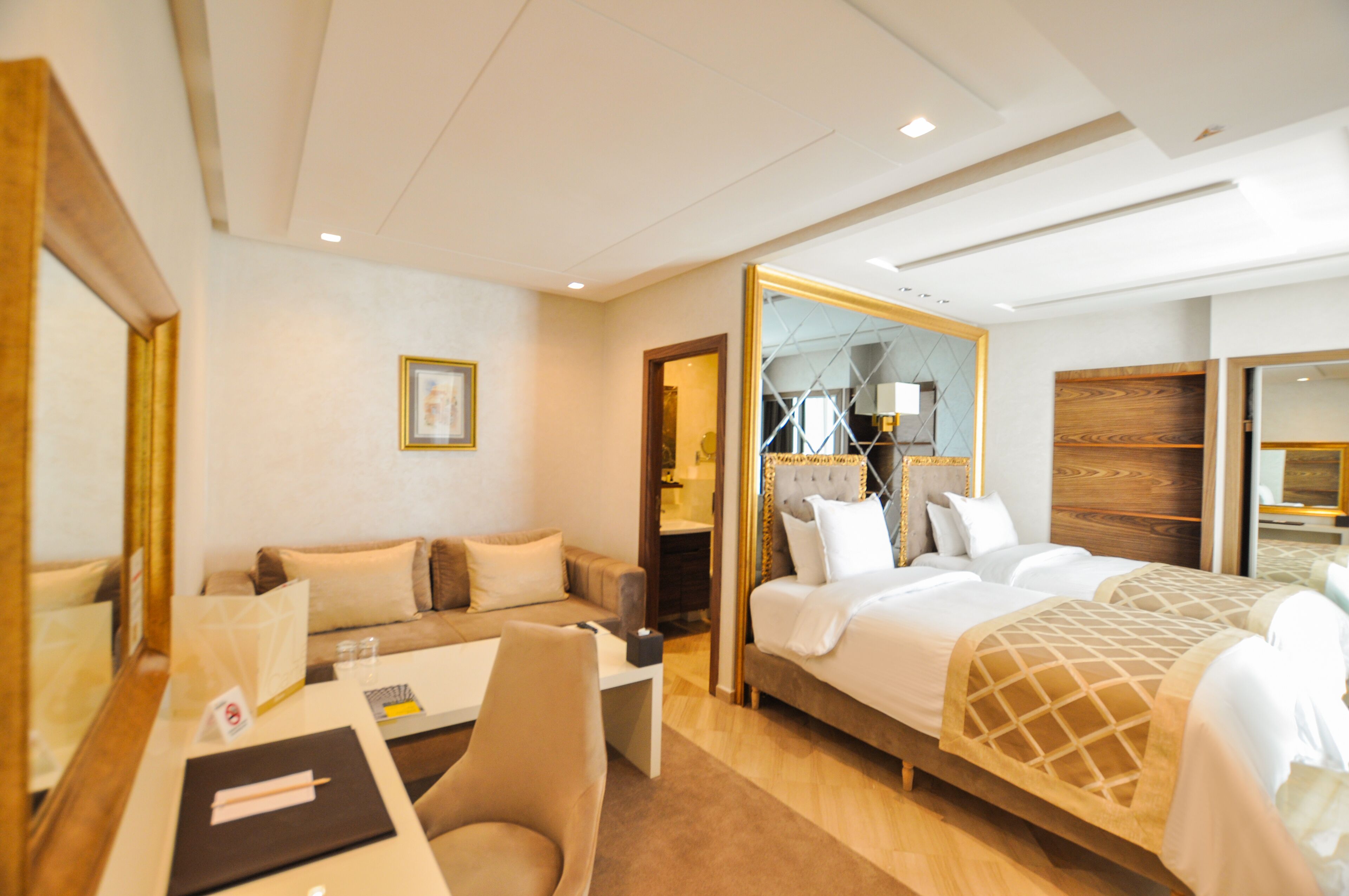 A hotel room with a bed, a sofa, a desk, and a mirror.