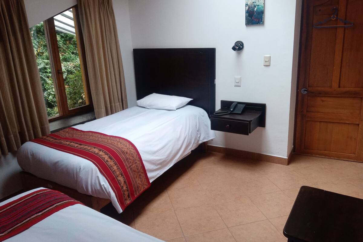 A hotel room with two beds, a nightstand with a phone, a wooden door, and a window with curtains.