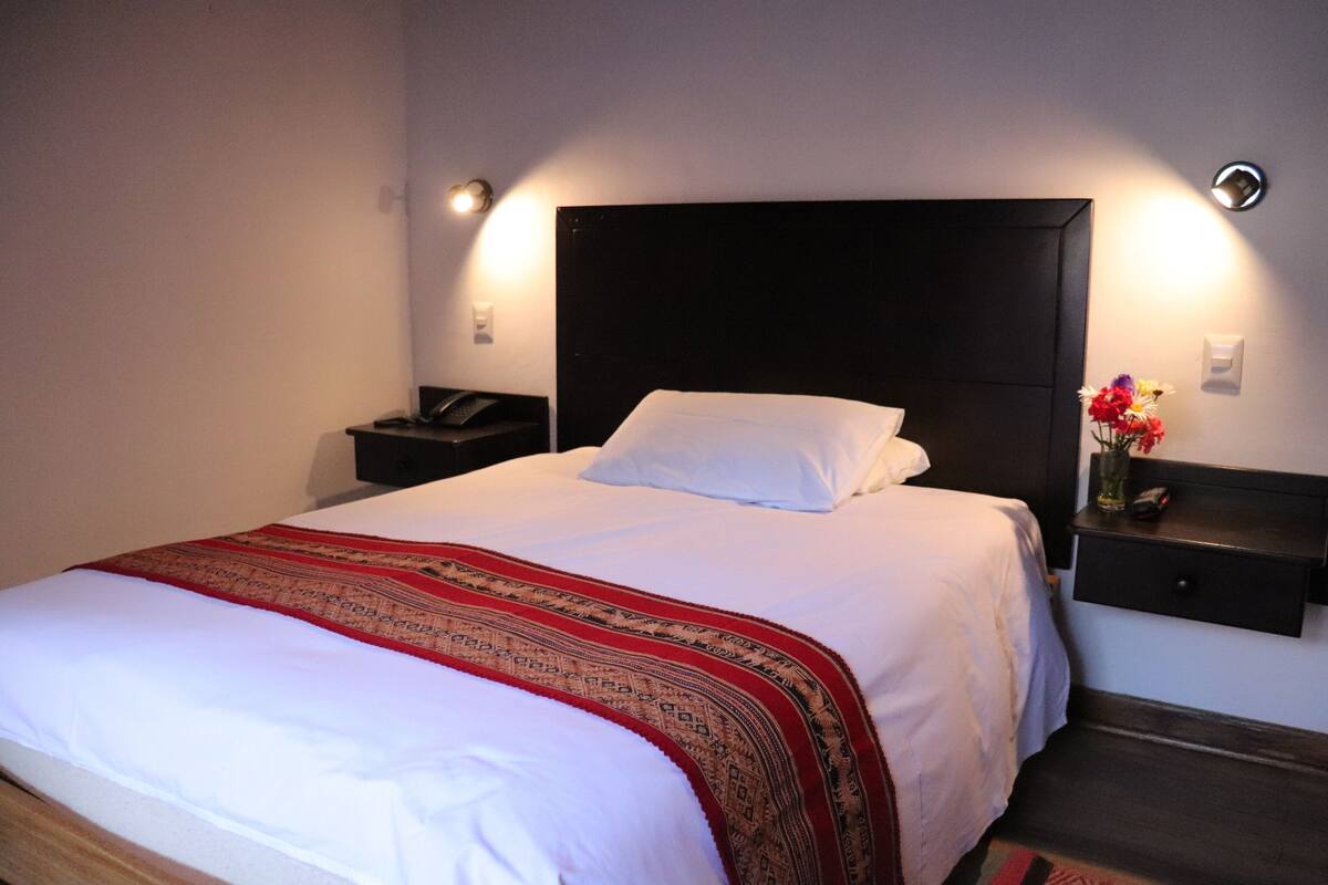 A neatly made bed with a white and red blanket, a black headboard, and bedside tables with lamps.