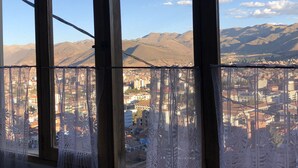 A view through a window with a lace curtain, featuring a cityscape and mountains in the background. - Hospedaje Turismo CAITH (Cusco)
