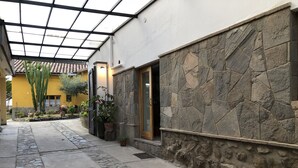 A covered outdoor area with stone walls, potted plants, and a yellow building in the background. - Hospedaje Turismo CAITH (Cusco)