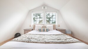 A bedroom with a large bed, two bedside tables, a window, and a ceiling fan. - Sea Breeze Cottages (Ocean Shores)