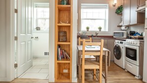 A kitchen with wooden cabinets, a washing machine, a microwave, and a dining area with a chair and table. - Sea Breeze Cottages (Ocean Shores)