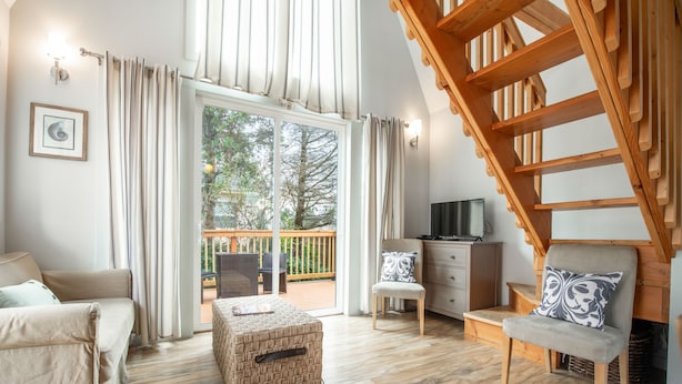 A cozy living room with a sofa, ottoman, and wooden staircase. - Sea Breeze Cottages (Ocean Shores)