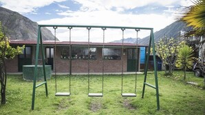 Eine Schaukelanlage in einer grünen Wiese, im Hintergrund ein Gebäude.