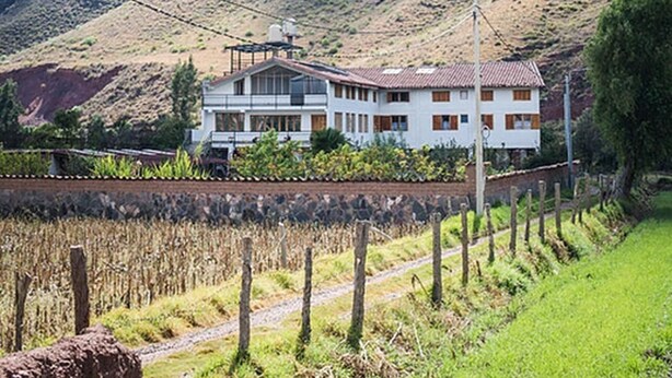 Ein zweistöckiges Haus mit geneigtem Dach, umgeben von einem Weinberg und einem Bergpanorama.