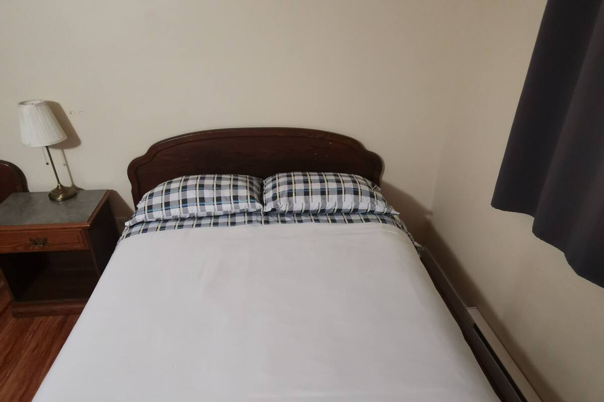 A single bed with a wooden headboard, a bedside table with a lamp, and a plain wall.