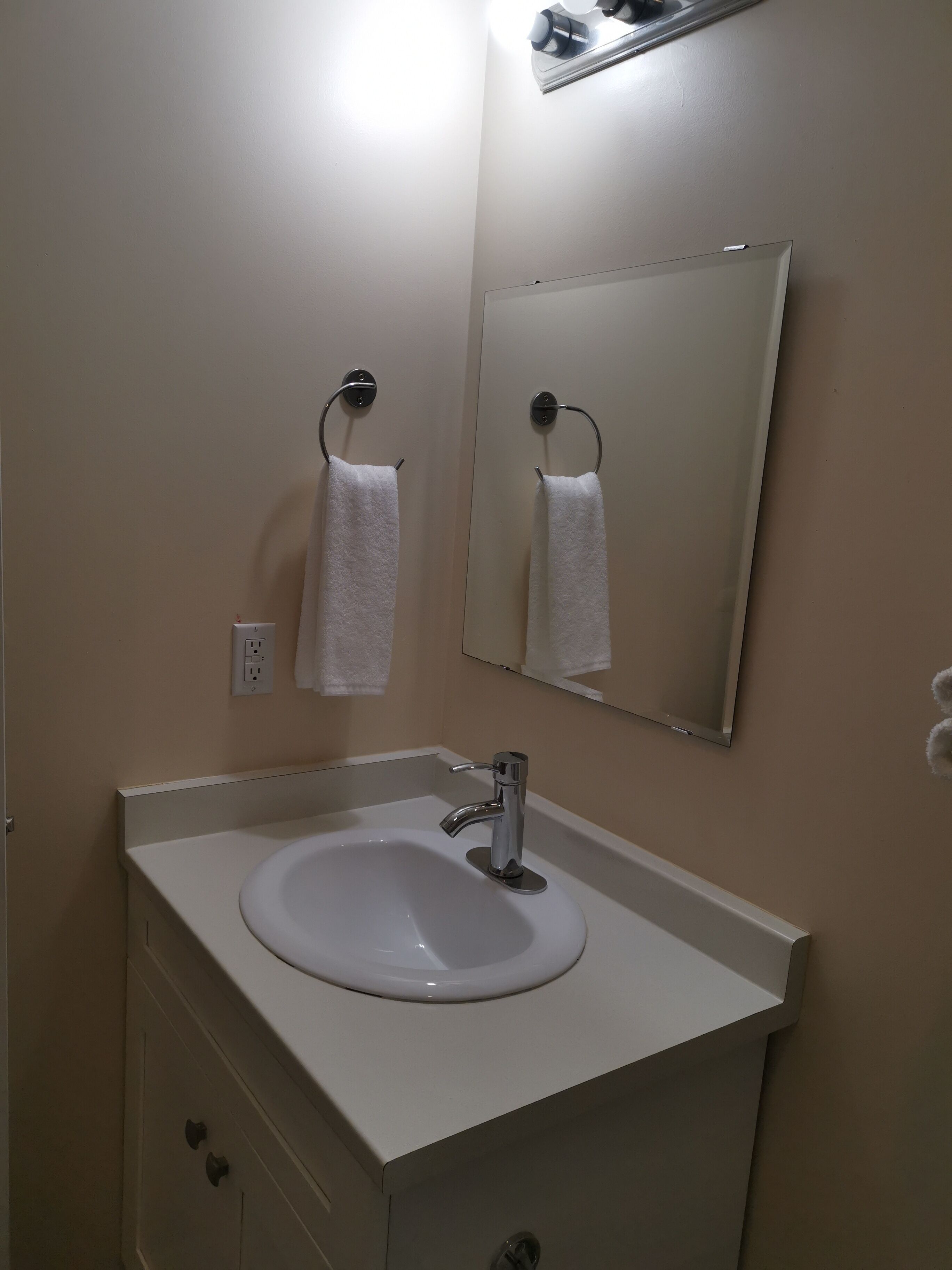 Un baño con un lavamanos blanco, un espejo y dos toallas colgadas en aros.