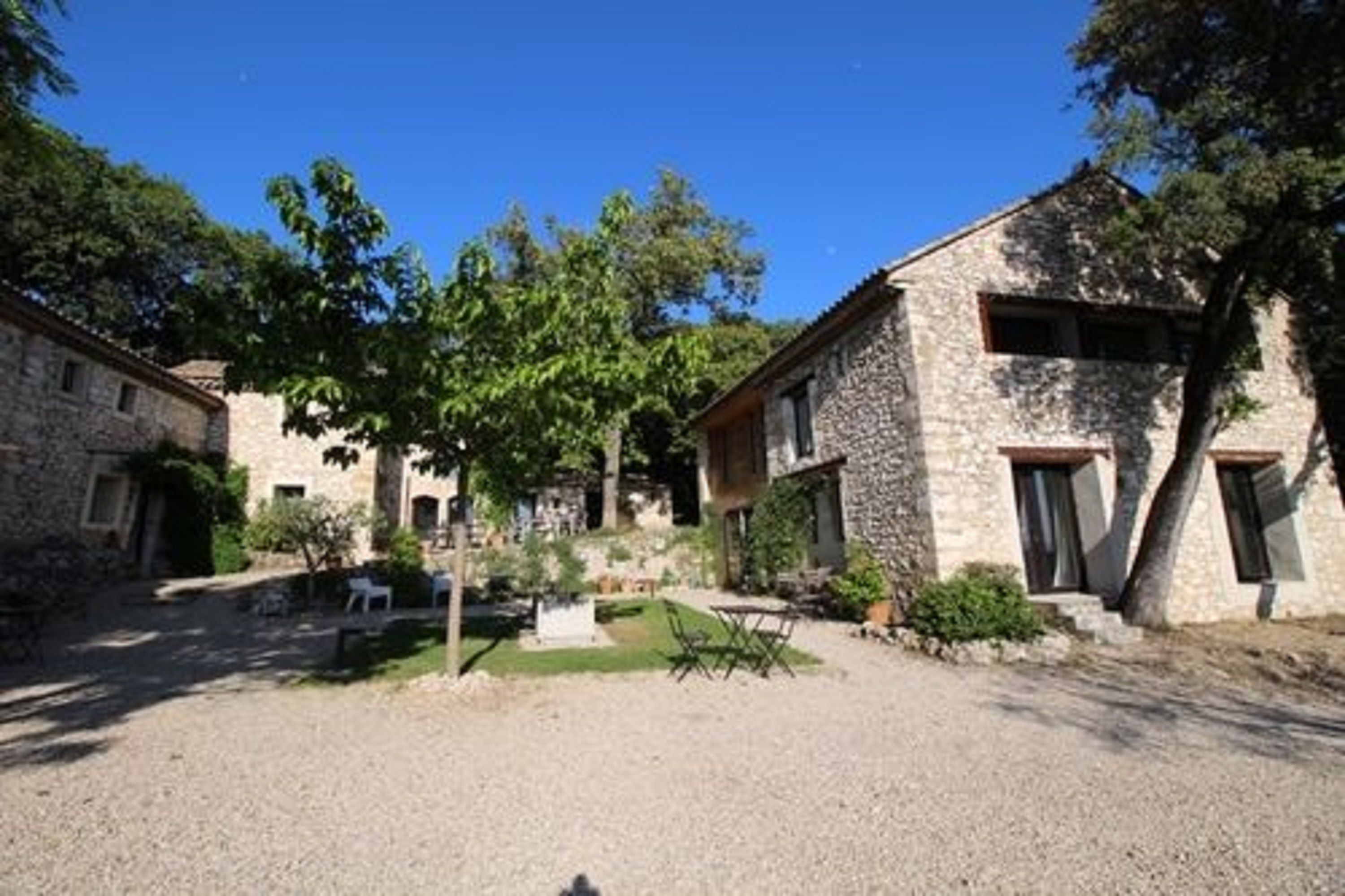 Un edificio de piedra con un patio de grava, un pequeño jardín y una mesa de madera.