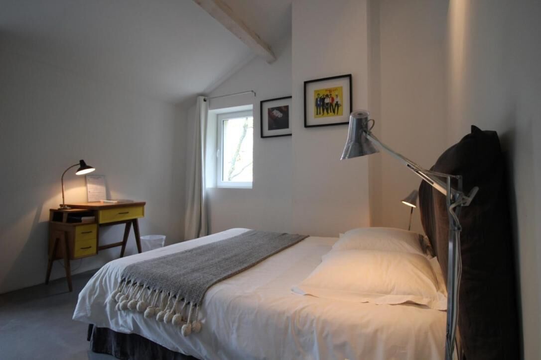 A bedroom with a bed, a desk, a lamp, and a window.