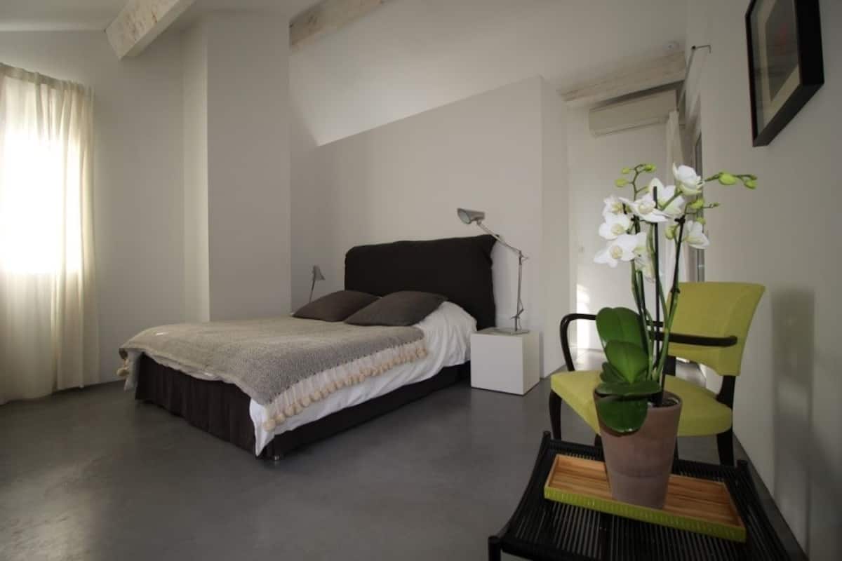 Ein Schlafzimmer mit Bett, Nachttisch, Lampe, Stuhl und einer Topfpflanze.