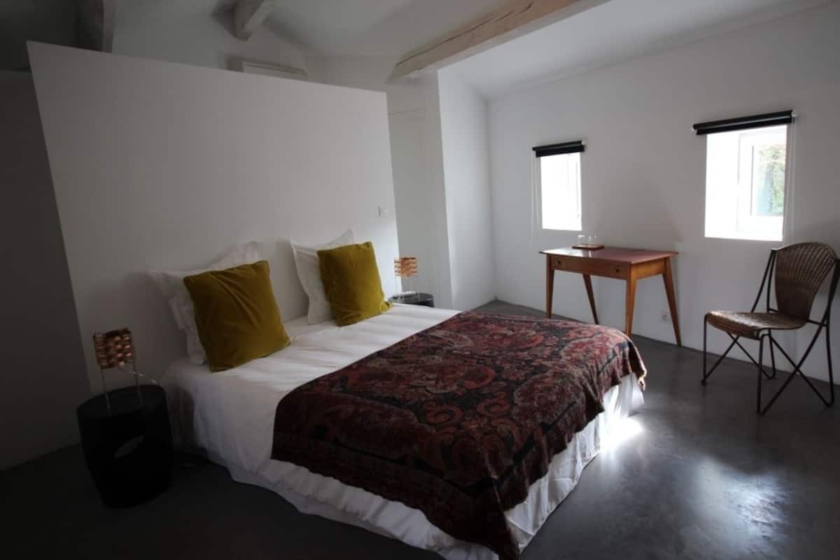 Ein Schlafzimmer mit einem Bett, einem Schreibtisch, einem Stuhl und zwei Fenstern.