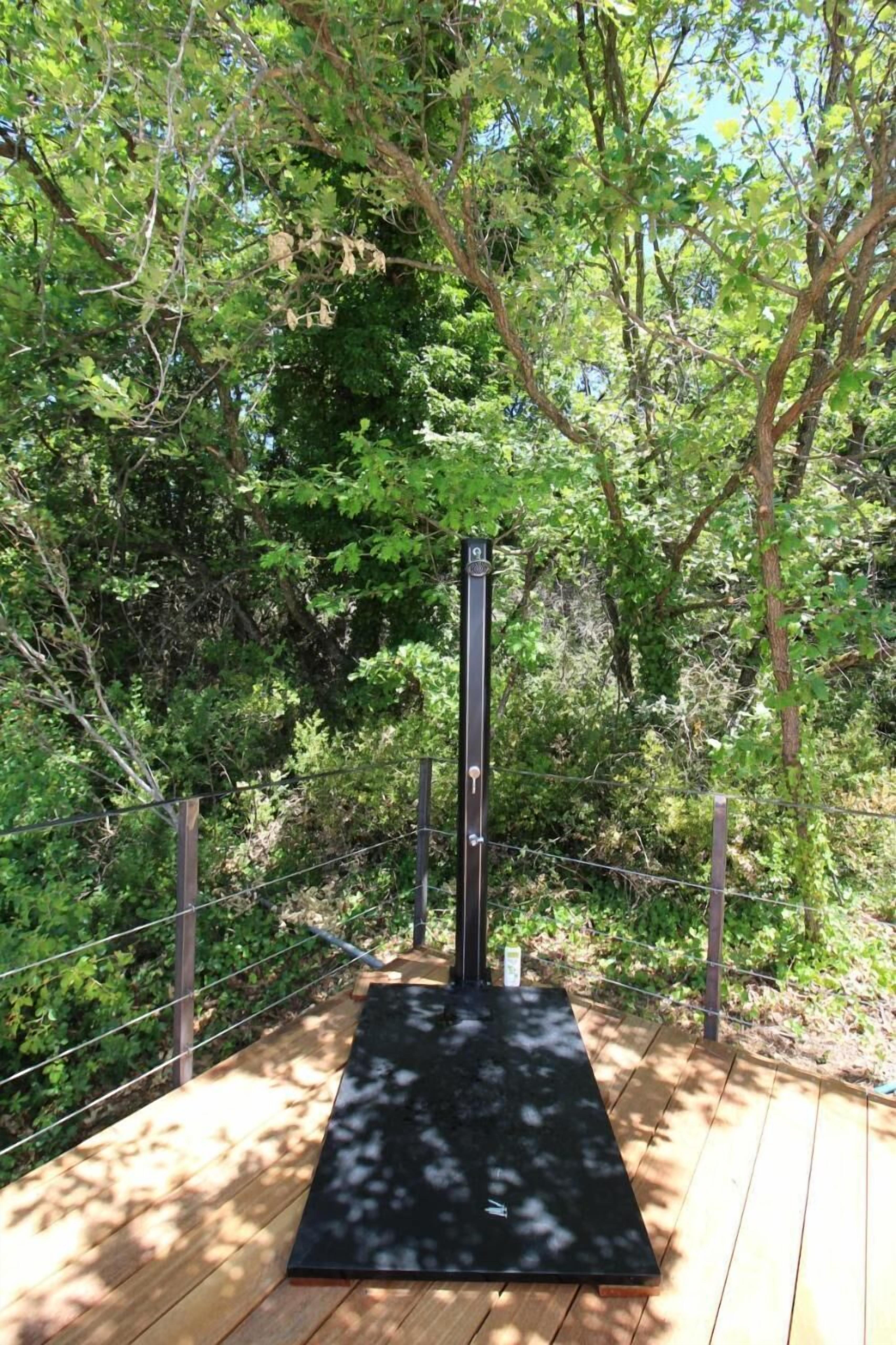 A wooden deck with a black exercise mat and a metal pole structure, surrounded by dense greenery.