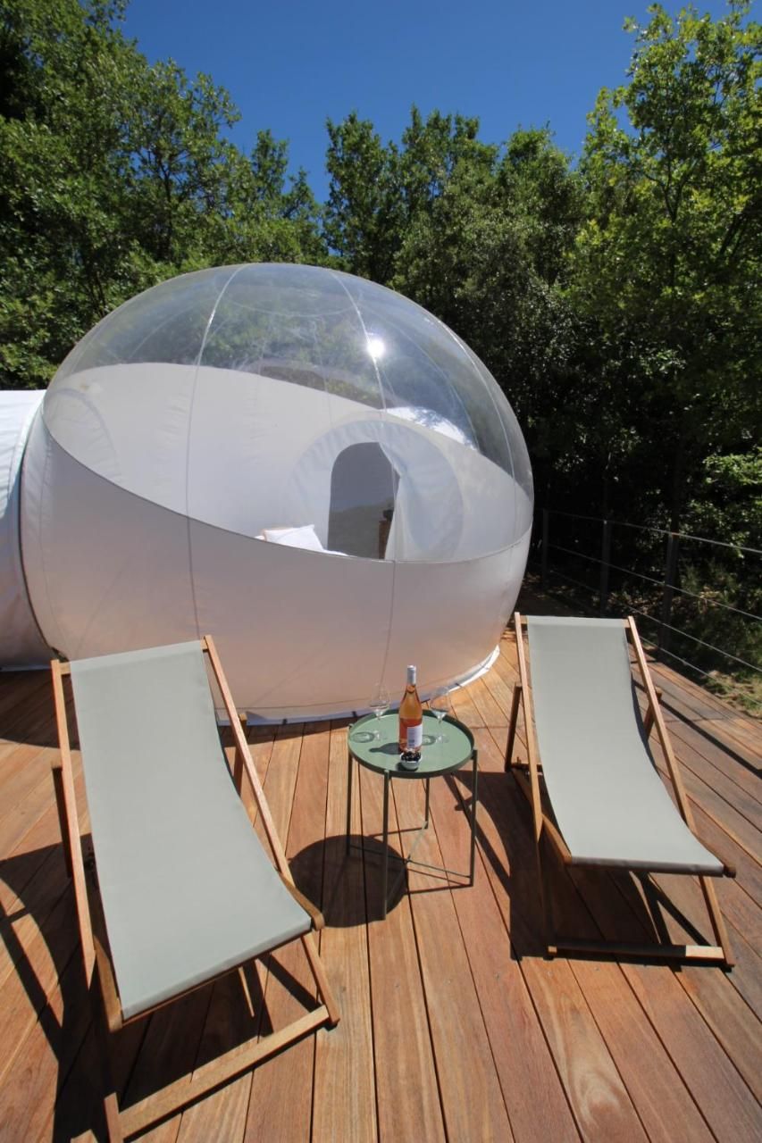 A transparent dome structure with a small table and two lounge chairs on a wooden deck.