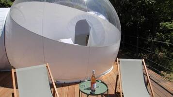 A transparent dome structure with a small table and two lounge chairs on a wooden deck.