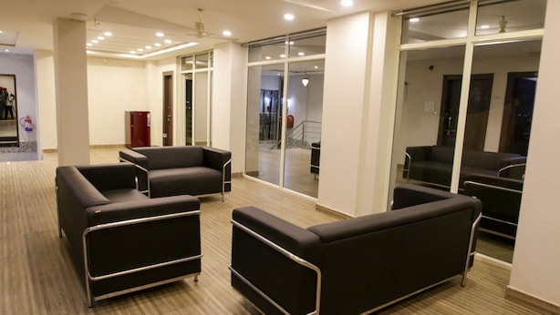 Un área de espera moderna con sofás de cuero negro, suelo de madera y puertas de cristal que dan a una escalera.