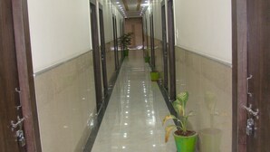 Un pasillo largo y bien iluminado con un suelo brillante, bordeado por puertas de madera y plantas en macetas verdes.