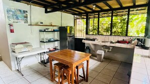 A kitchen with a wooden table and stools, tiled floor, and a window with greenery outside.