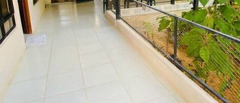 A covered outdoor area with tiled flooring, a metal railing, and potted plants.