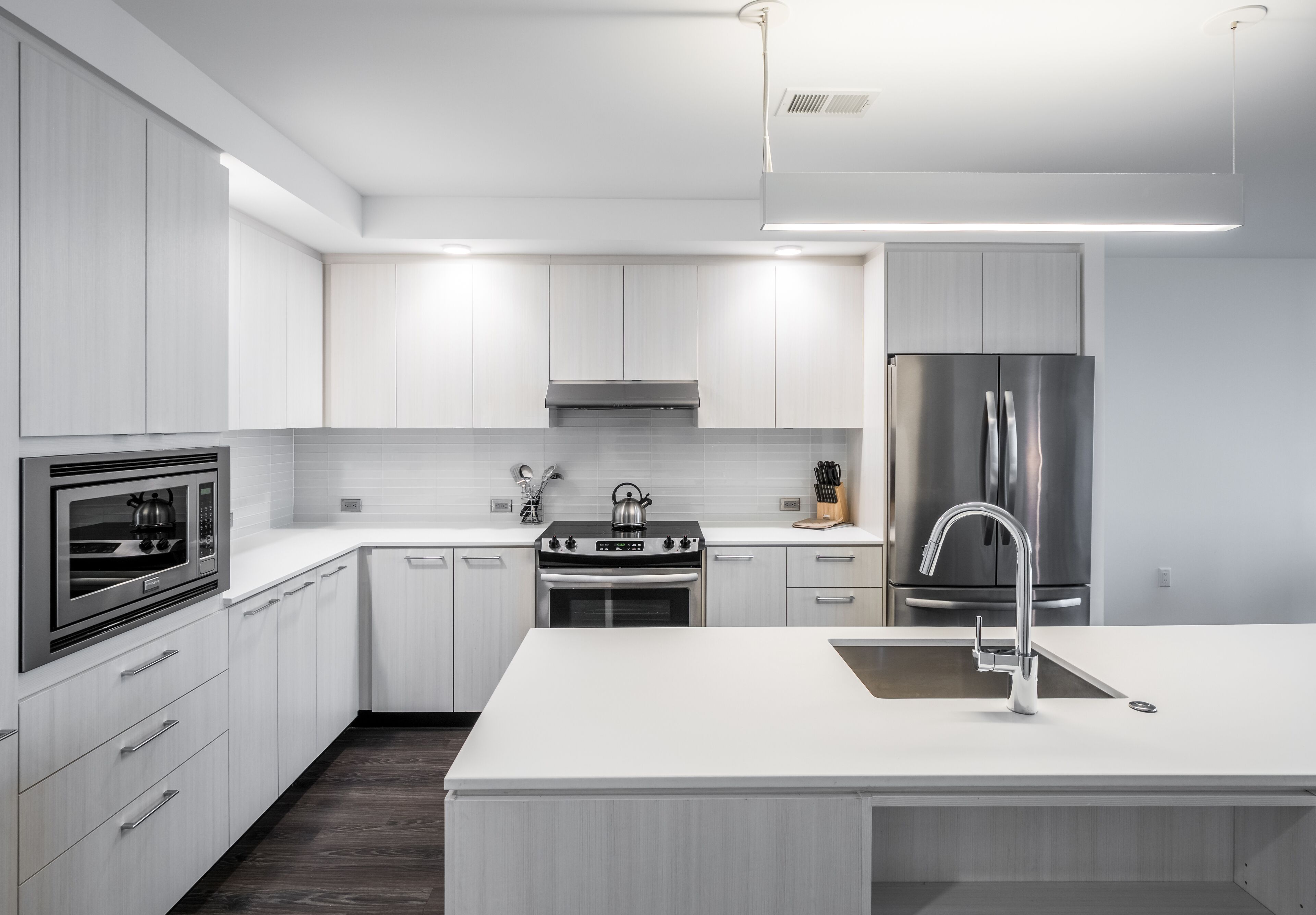 A modern kitchen with white cabinetry, stainless steel appliances, and a central island with a sink.