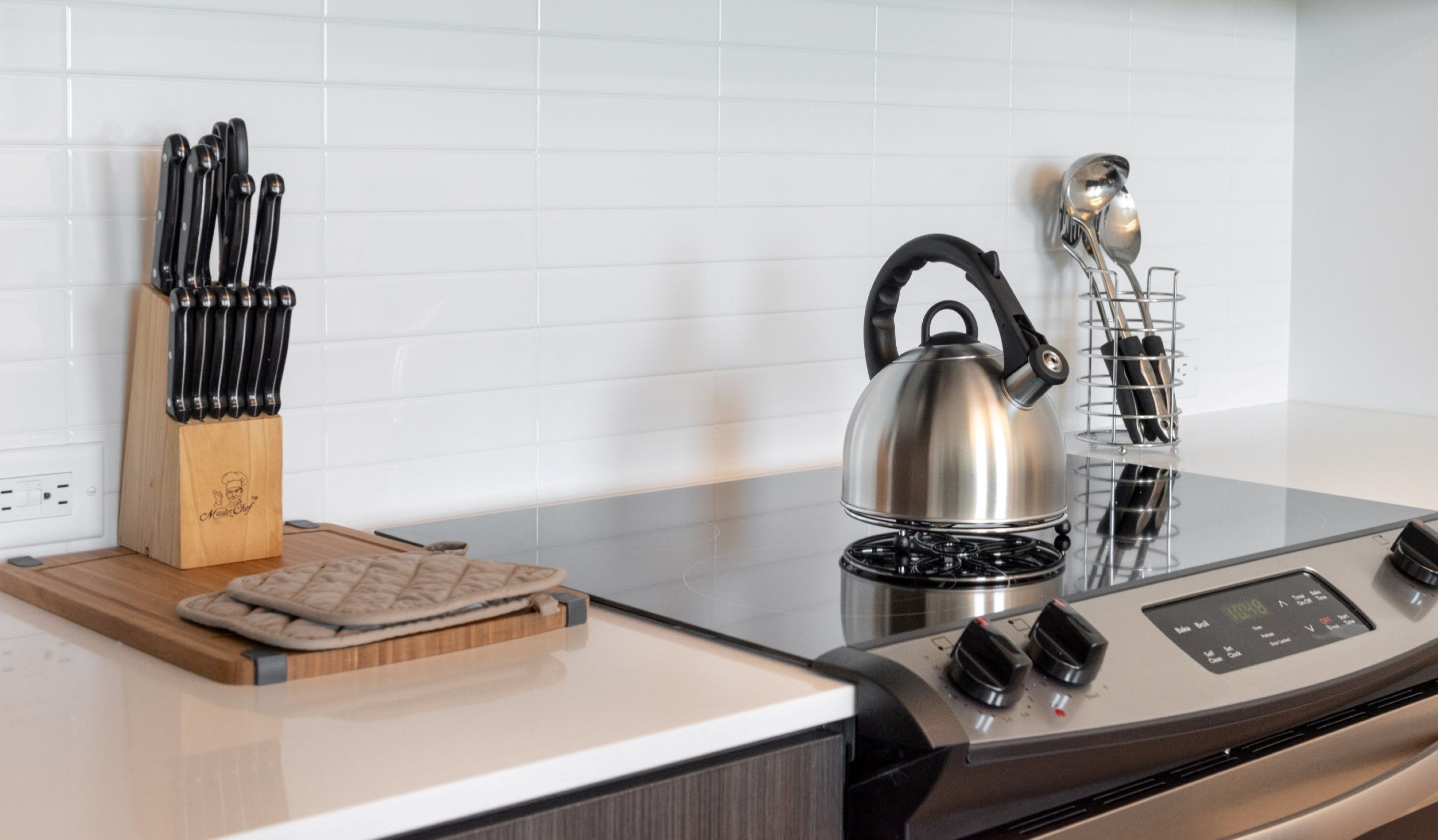 A kitchen with a stainless steel kettle, a knife block, and a modern stove.