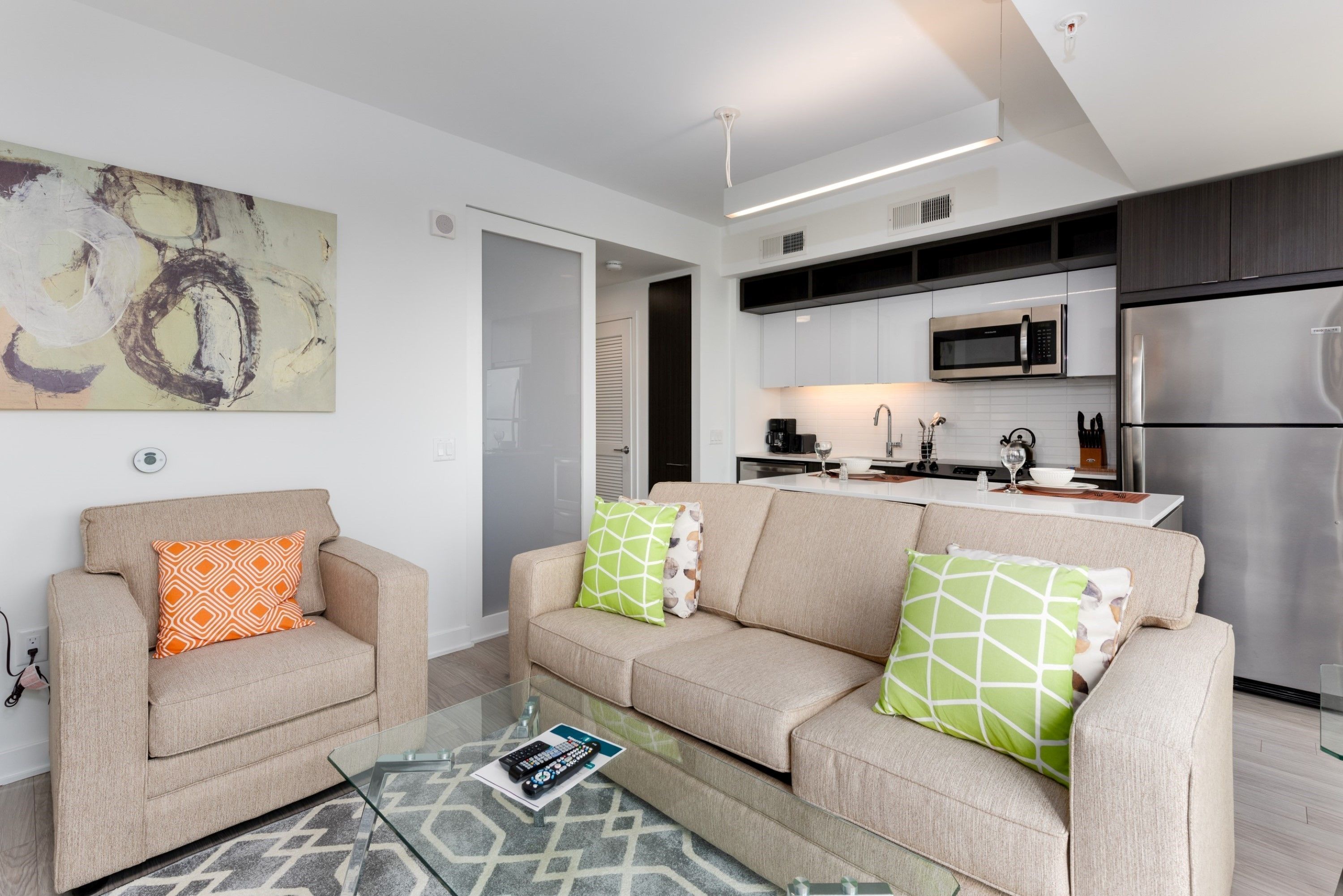 Uma sala de estar moderna com sofá e mesinha de centro, cozinha com eletrodomésticos de aço inoxidável e um grande quadro abstrato na parede.