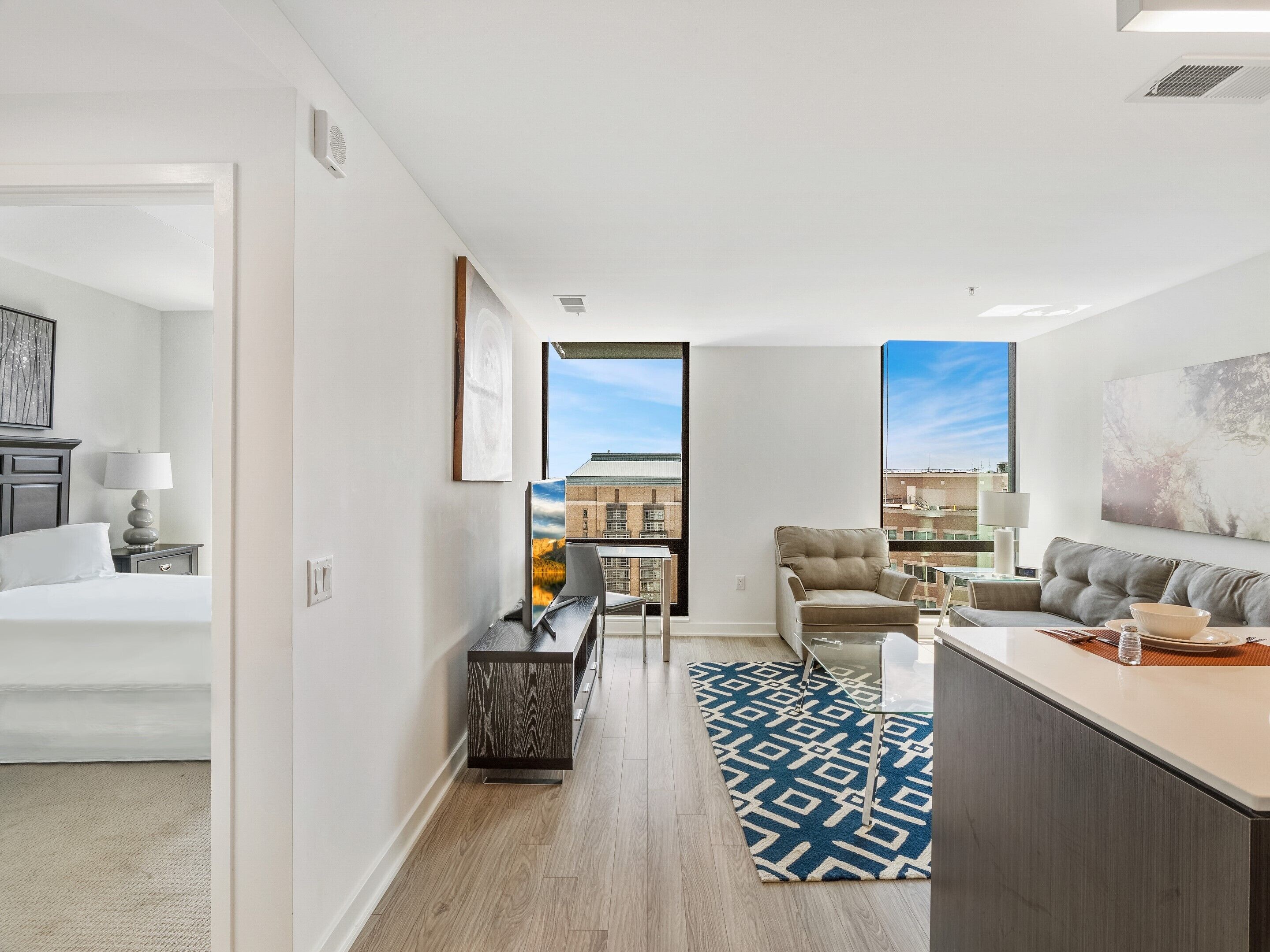 Une chambre d’hôtel moderne équipée d’un lit, d’un bureau, d’une chaise, d’un canapé et d’une grande fenêtre donnant sur la ville.
