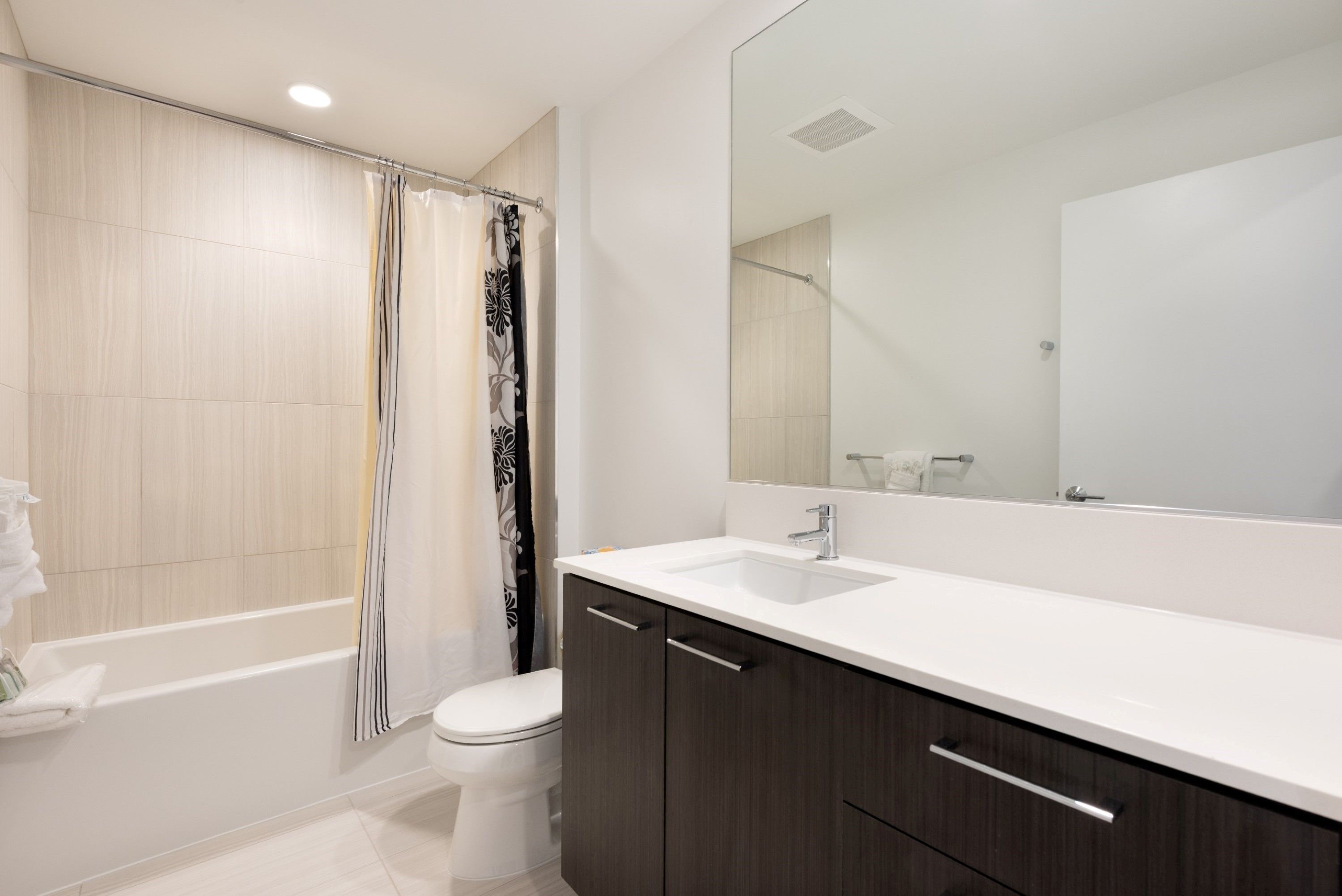 A modern bathroom with a bathtub, toilet, and a large mirror above the sink.