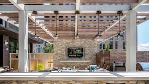 An outdoor bar area with stone walls, a flat-screen TV mounted on a stone wall, and a wooden ceiling structure.