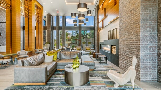 A spacious lobby with a modern design, featuring a large seating area, a fireplace, and large windows offering a view of the outdoors.