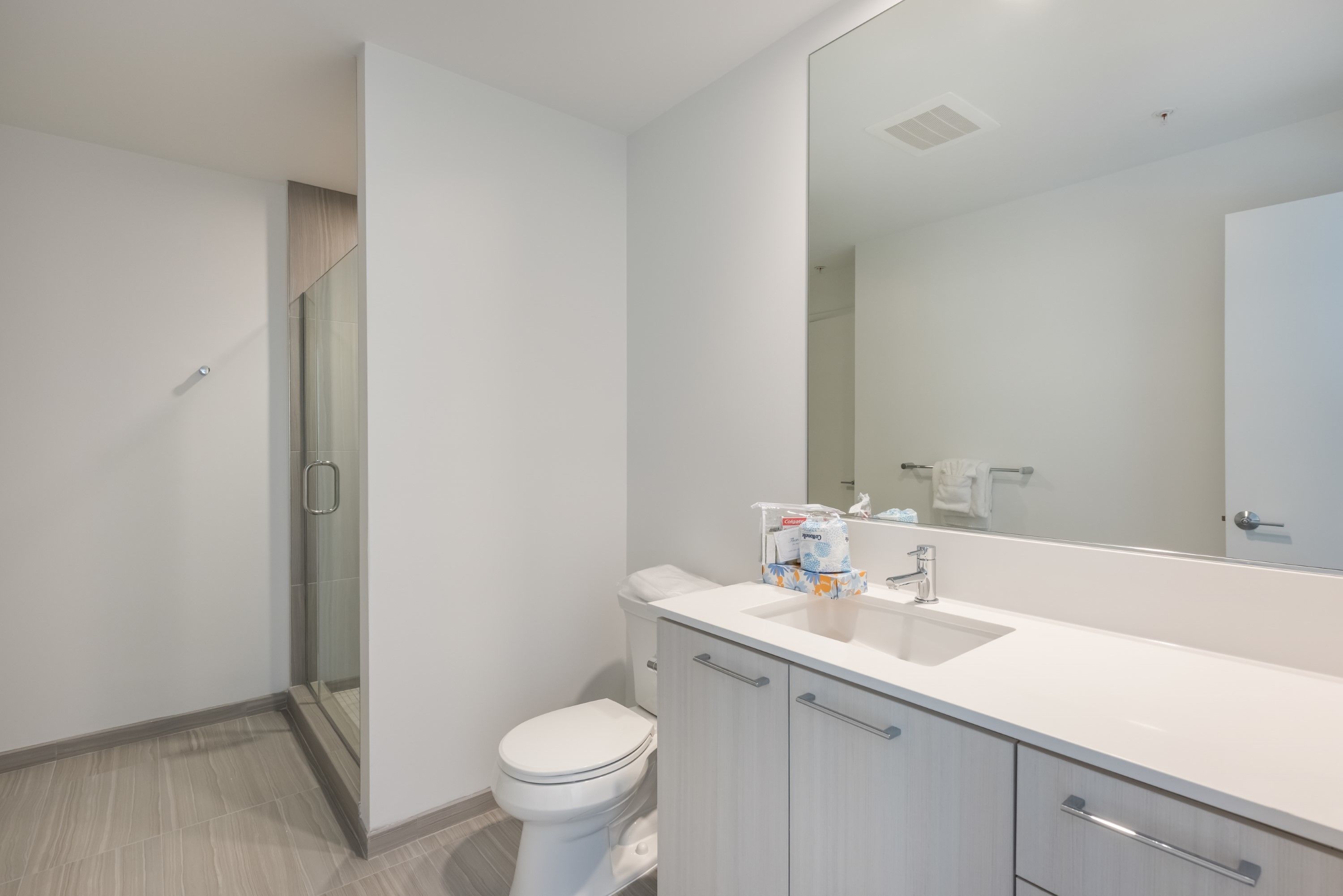 Een moderne badkamer met een wit toilet, een douchecabine van glas en een grote spiegel boven de wastafel.